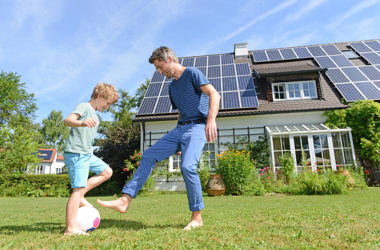 Vater und Sohn spielen vor einem Haus mit Photovoltaik-Anlage